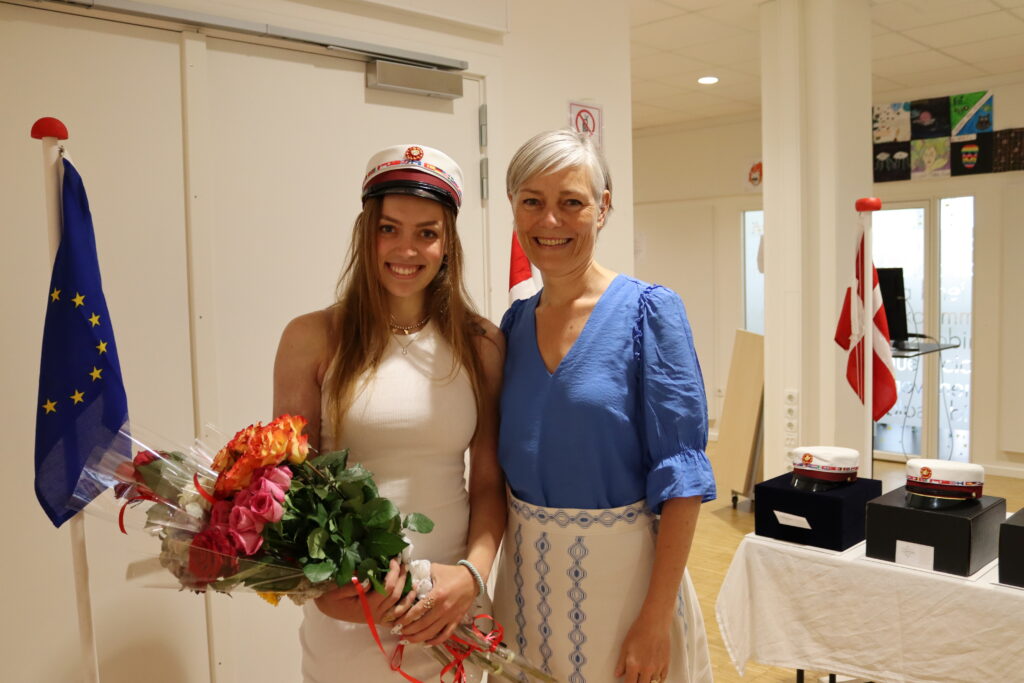 Director Julie Rørdam Thom with the first ever Euroepan Baccalaureate student from ESCPH in 2023, Sofie. The student is wearing her graduation hat and holding a bouquet of flowers.